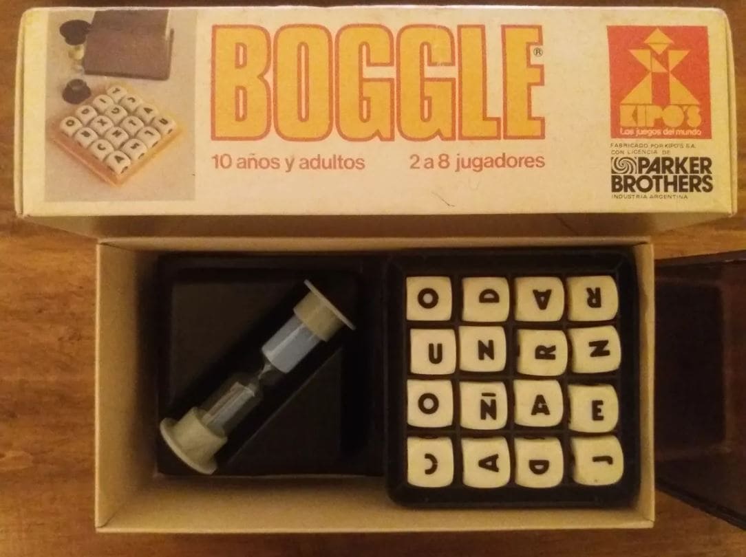 A vintage Boggle game set featuring a sand timer and lettered dice in a grid.