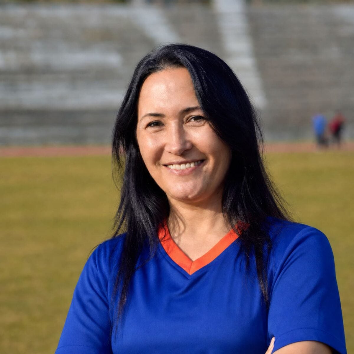 Prof. Dr. Canan Koca smiling outdoors beside an athletics field