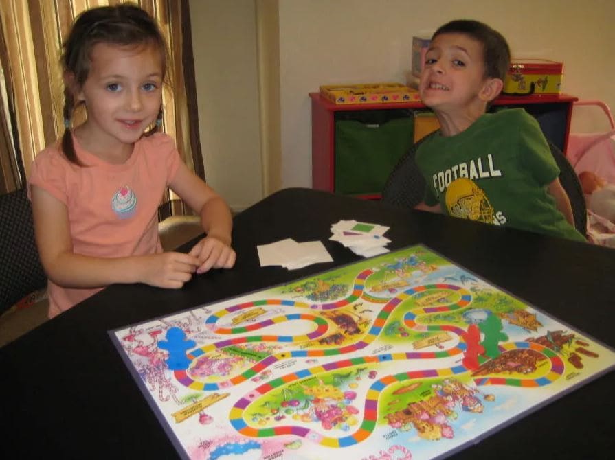 Two children smiling while playing a colorful Candy Land board game.