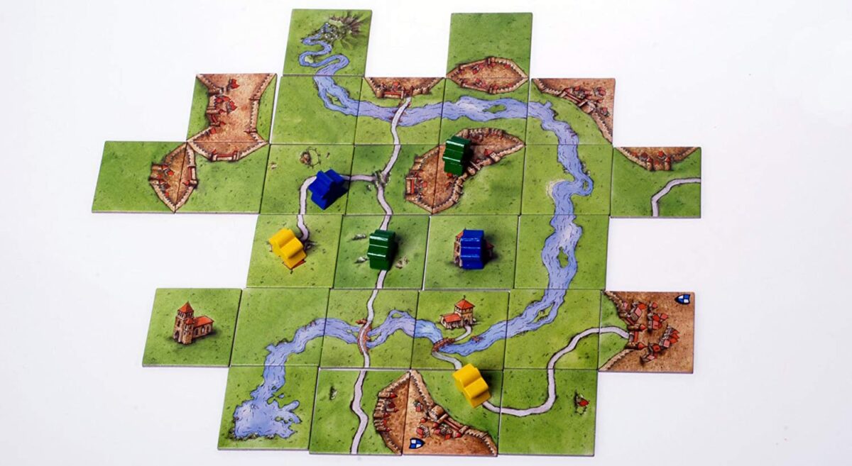 A solo setup of the Carcassonne board game, with tiles featuring fields, cities, roads, and rivers, and several meeples placed on the tiles.