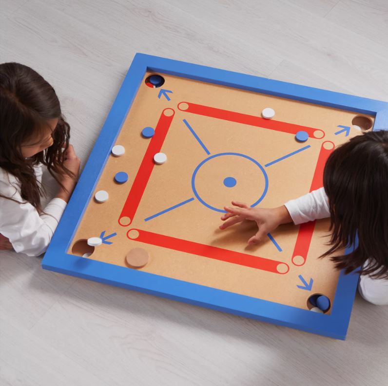 Two children playing carrom, a traditional board game, on the floor.