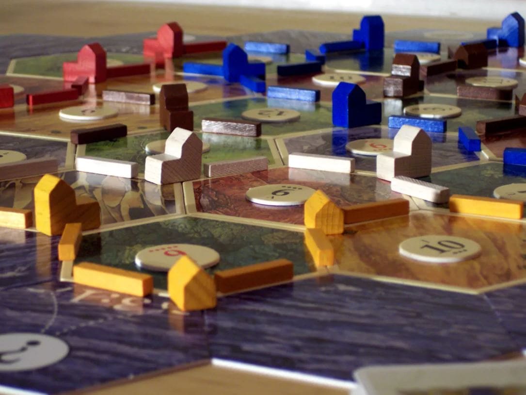 Close-up of wooden game pieces on a Catan board, featuring settlements and roads.