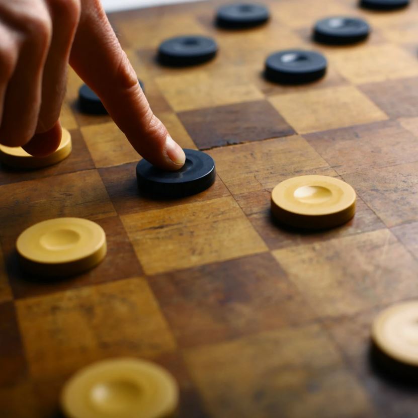 Close-up of a person moving a piece on a checkers board.