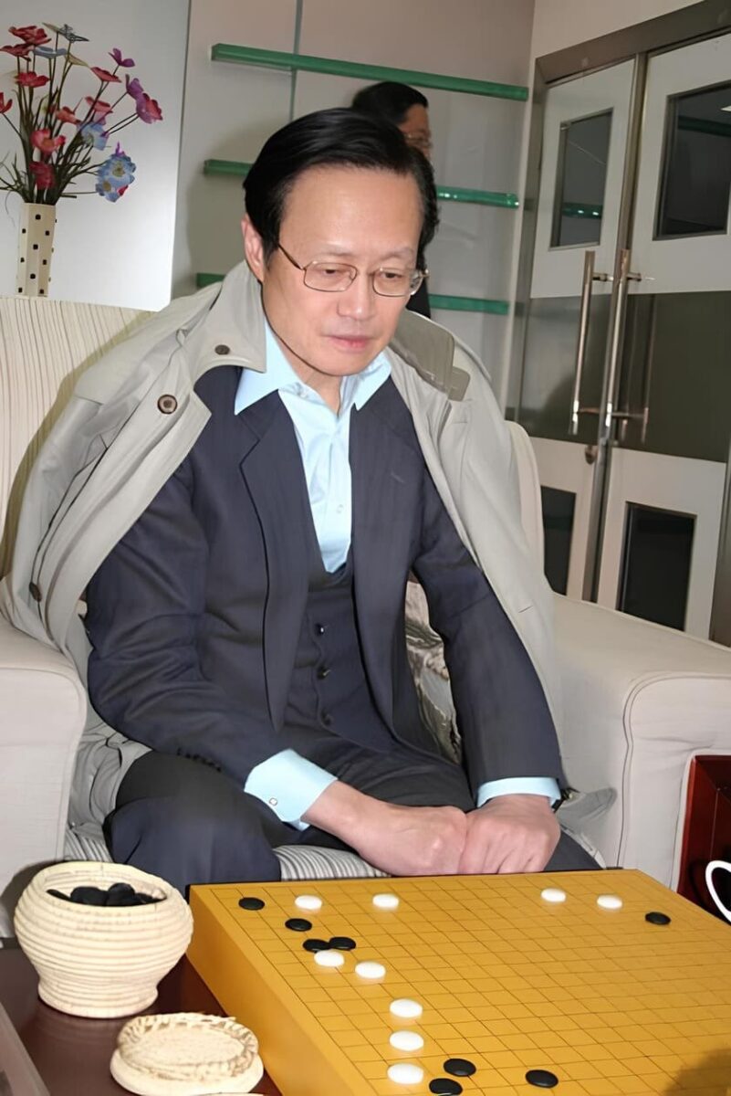 Chen Zude sitting in a suit, thoughtfully observing a Go board during a game.