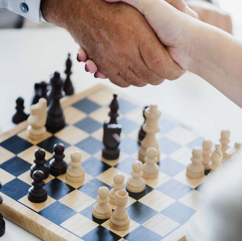 Two people shaking hands over a chess board, with pieces in mid-game.