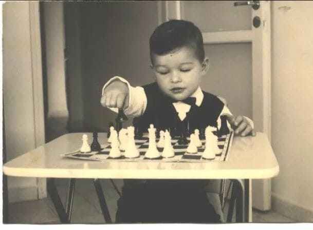 A vintage black-and-white photo of a young child focused on playing a chess game.