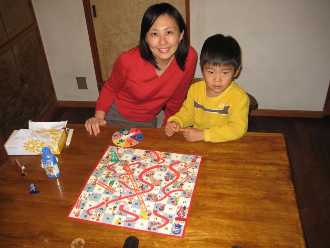 A mother and her son playing Chutes and Ladders, sitting at a wooden table.