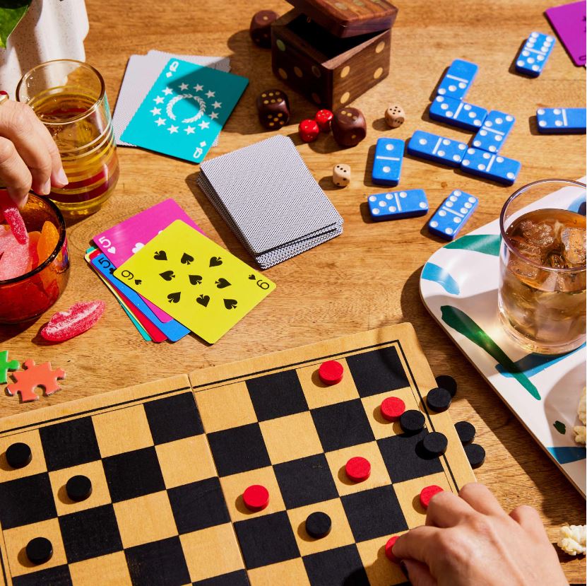 A table with various classic board games, including cards, dominoes, and checkers, being played.