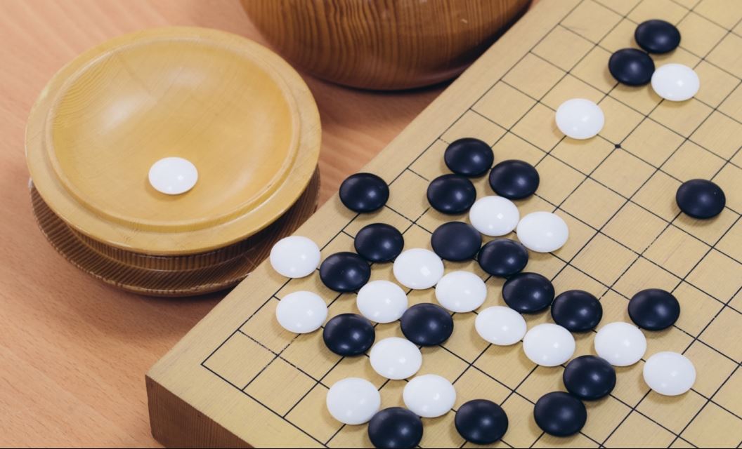 A Go board with a complex position in the upper-left corner on a 19x19 grid. Black and white stones are tightly clustered along the top and left edges, creating a tense situation.