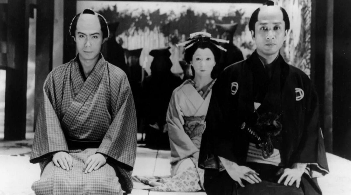 A black-and-white film still from 'Double Suicide' featuring two men in traditional Japanese clothing, seated formally with a woman in traditional attire in the background.