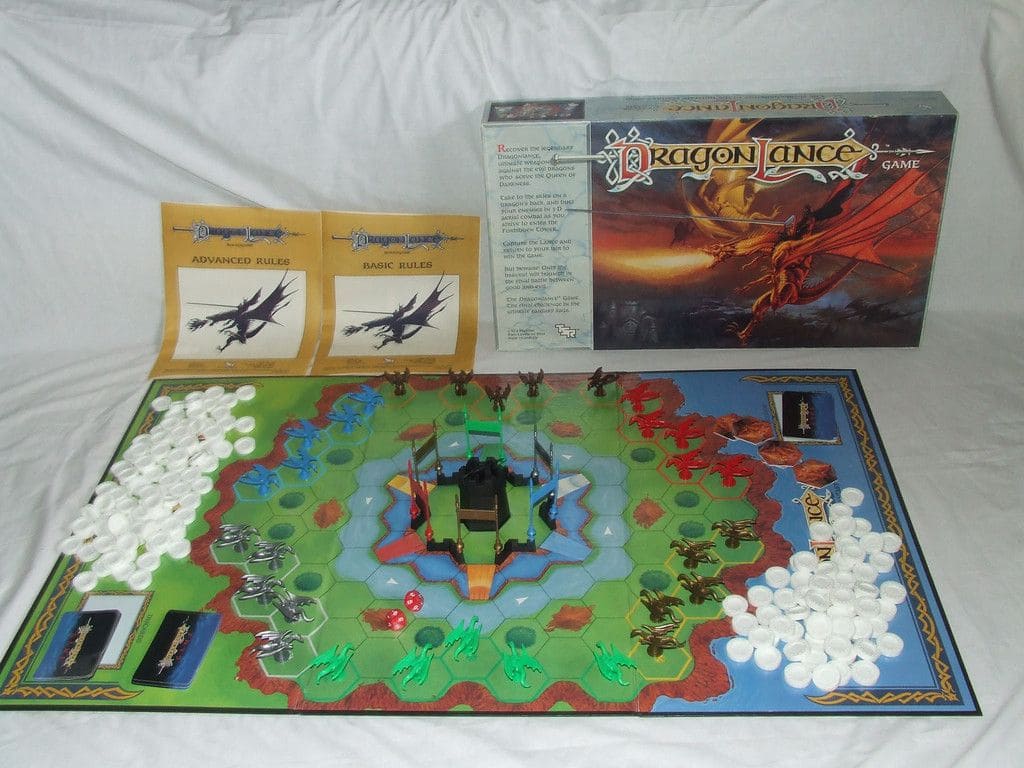 The Dragonlance board game laid out with the game board, dragon miniatures, tokens, and rulebooks, with the game box featuring a dragon in flight.