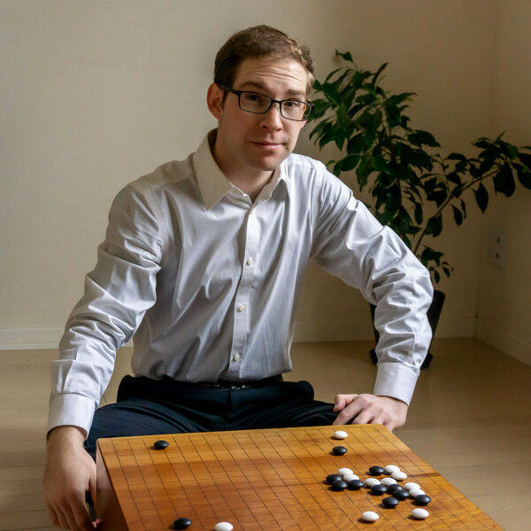 A man in a white shirt sitting beside a Go board in a home setting