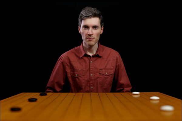 A man sitting behind a Go board with black and white stones, looking directly ahead