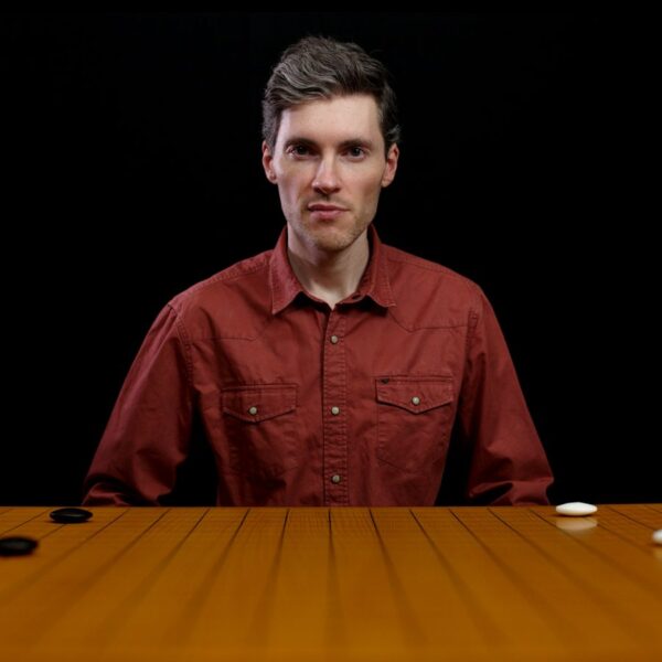 A man sitting behind a Go board with black and white stones, looking directly ahead