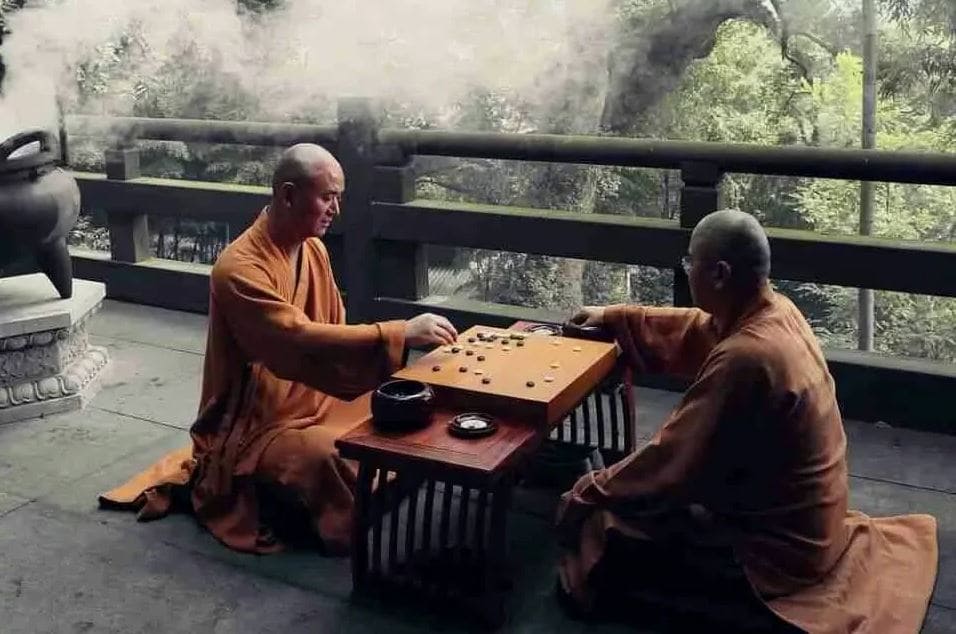 Two monks sitting outdoors, playing the traditional game of Go, symbolizing mindfulness and focus.