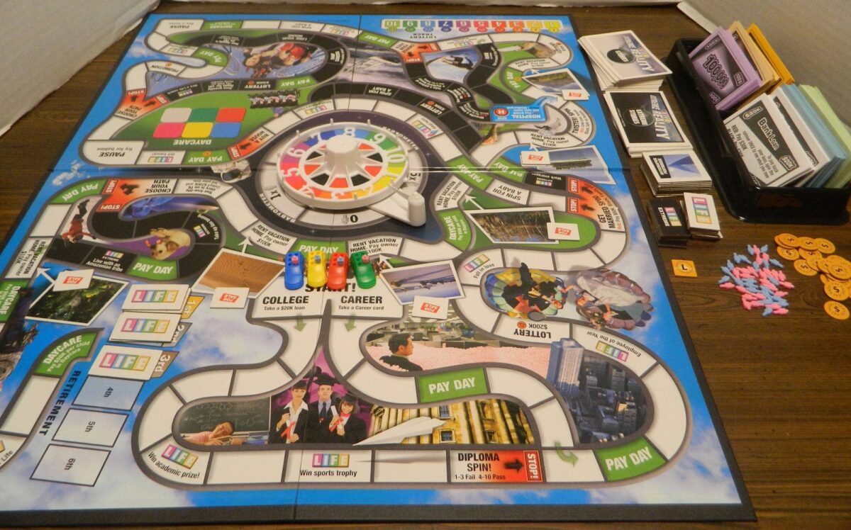 The Game of Life board game, showing colorful pathways, the signature spinning wheel, and player pieces, along with money and cards organized for a family game session.