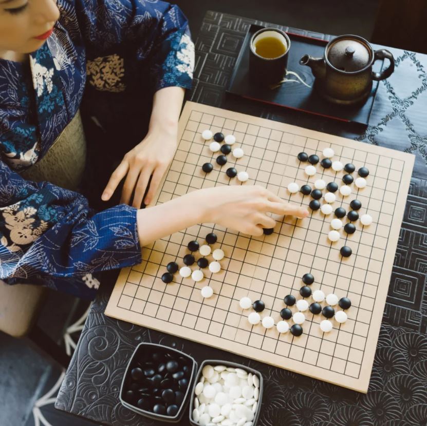 A person in traditional attire playing Go, with a detailed Go board and stones.