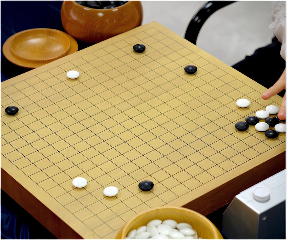 Close-up of a Go board with opening positions, bowls of stones, and a hand making a move.