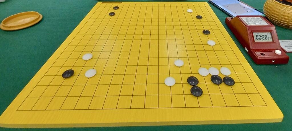 Yellow Go board on green table with stones and clock, made from medium-density fiberboard