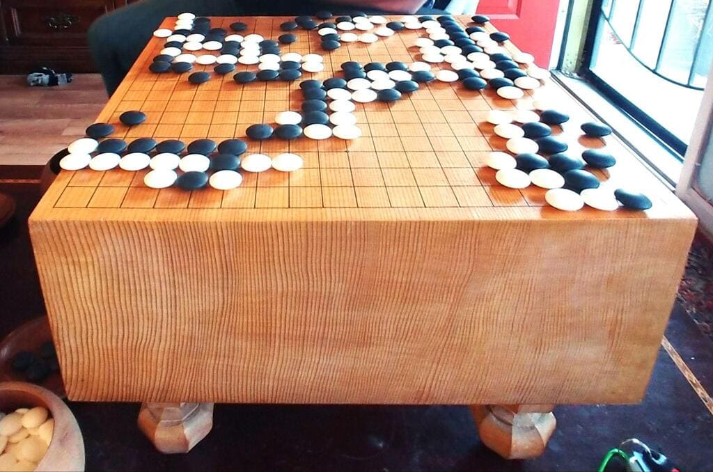 Large Go board with tight, distinct tree ring pattern and an ongoing game in progress
