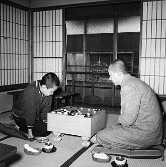 A historical black-and-white photo of Go Seigen teaching a young Rin Kaiho during a Go training session in a traditional Japanese tatami room.