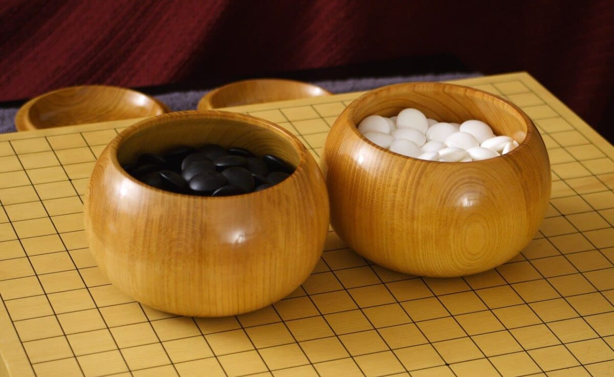A set of black and white Go stones in elegant wooden bowls, placed on a traditional wooden Go board.