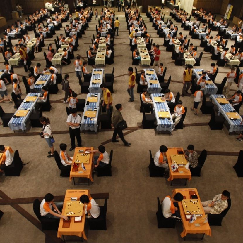 A large hall filled with players at tables competing in a Go tournament.