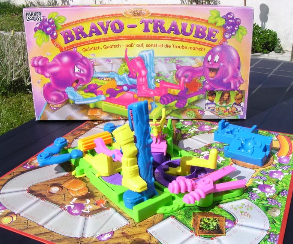 A colorful setup of the Grape Escape board game with vibrant purple grape-themed characters and mechanical traps on a lively game board.