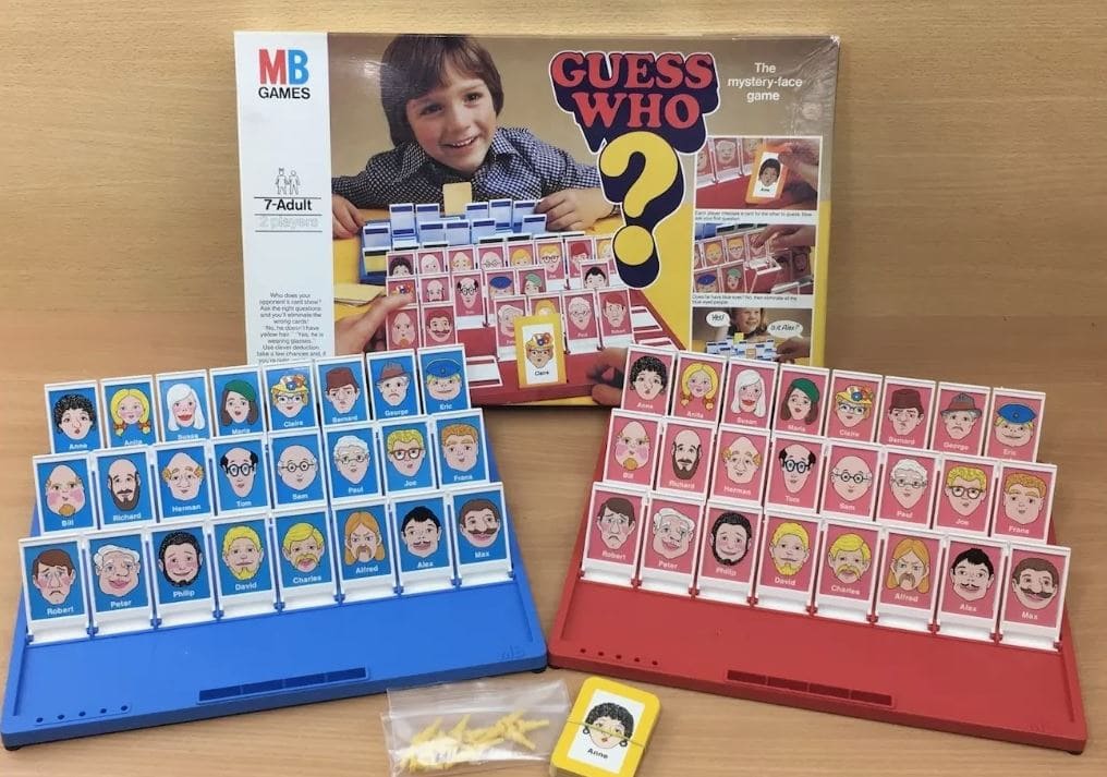 Guess Who board game with red and blue boards showing various character cards, along with the game box featuring a child holding a character card.