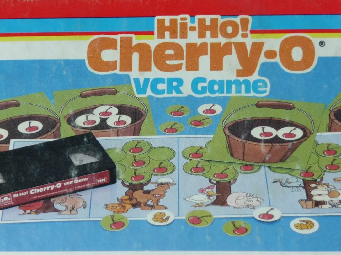 A nostalgic Hi-Ho Cherry-O VCR game box, featuring cherry trees and animal illustrations, alongside a VHS tape for interactive gameplay.