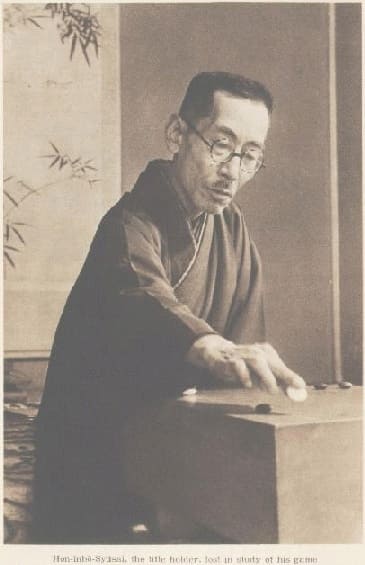 Honinbo Shusai intently studying a Go board, captured in a sepia-toned portrait that highlights his concentration and traditional attire.