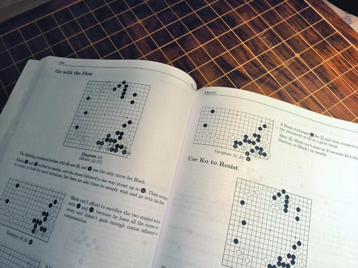 A Go strategy book open to a page titled 'Go with the Flow,' showing Go board diagrams and advice on using ko to resist, placed on a wooden Go board.