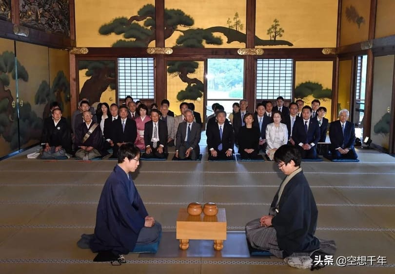 Iyama Yuta and his opponent preparing to play a Go match in a historic Japanese room with a seated audience behind them