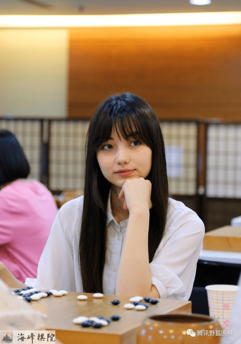 Joanne Missingham in a white shirt, sitting at a Go board with a thoughtful expression, resting her chin on her hand.