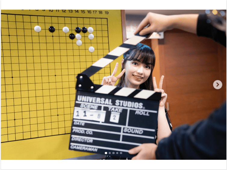 oanne Missingham posing with a clapperboard in front of a Go board, smiling and making a peace sign during a Go promotion.