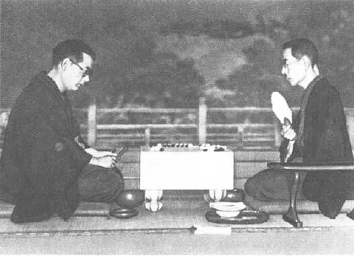 A historical photograph of two Go players in traditional attire engaging in a match on a classic Japanese Go board.