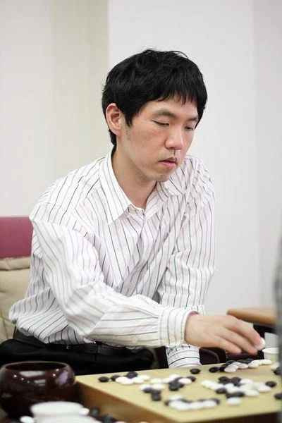 Lee Changho in a striped shirt, intensely focused as he plays a game of Go, carefully placing stones on the board.