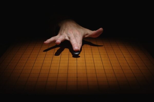 A hand placing a black Go stone on a traditional wooden board