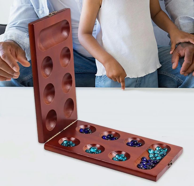 A Mancala board with marbles, with a child and an elder playing in the background.