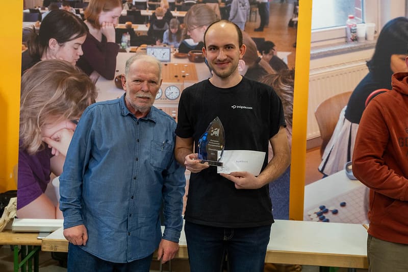 Mateusz Surma holding a Go tournament trophy and certificate, standing beside European Go Federation President Martin Stiassny at an award ceremony.