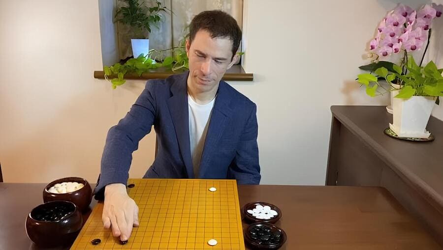 Michael Redmond analyzing a Go game at home with Go bowls and stones neatly arranged on the table.