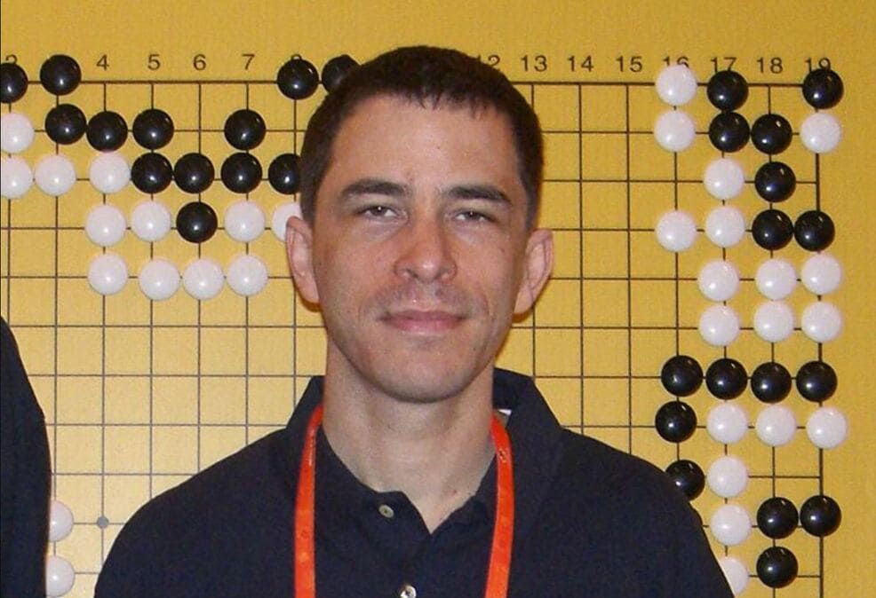 Michael Redmond posing in front of a Go board during a professional Go tournament.