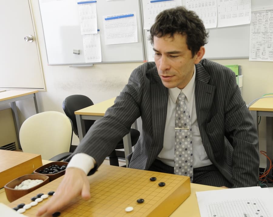 Michael Redmond in a professional setting, teaching Go strategies and demonstrating moves on a board.