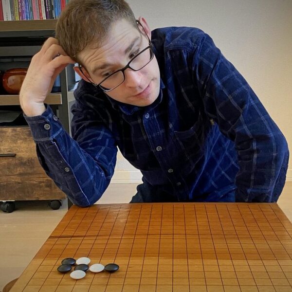 A young man in glasses leans over a Go board studying a life-and-death problem