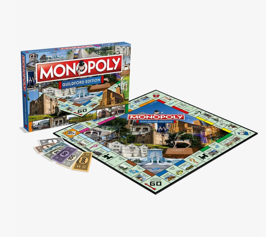 A Monopoly board game set up with property cards, money, and game pieces, including the Guildford edition box.