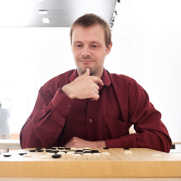 Man in a red shirt thinking deeply over a Go board during a competition