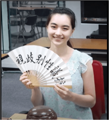 Joanne Missingham holding a fan with Chinese text, protesting gender discrimination in Go, smiling while sitting at a Go board.