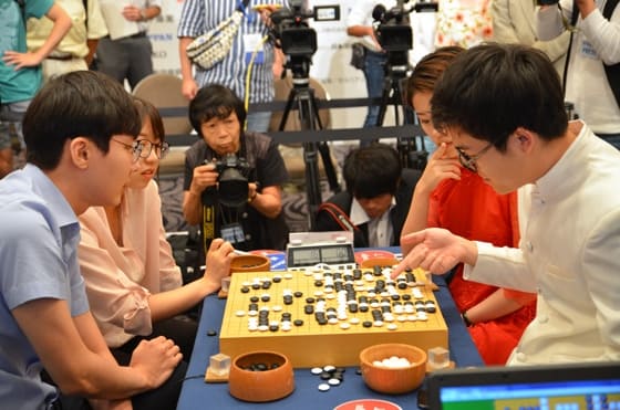 A group of players engaged in a Rengo match, a team-based variation of Go, with commentators analyzing the game.