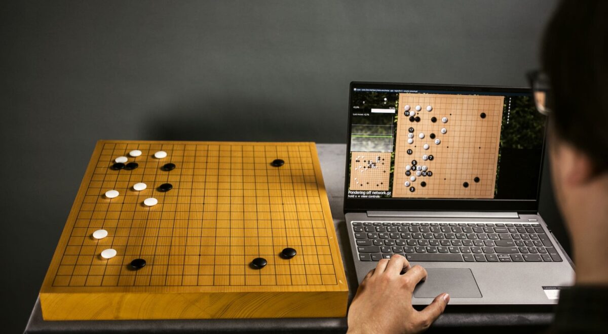 A player analyzing a Go game using both a physical board and a computer program.