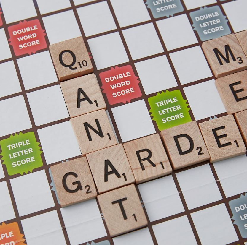 A close-up of a Scrabble board with tiles forming the words "QANAT" and "GARDEN".